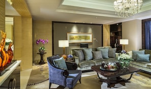 A modern living room with a sofa, armchair, and coffee table, featuring a chandelier and artwork on the wall.