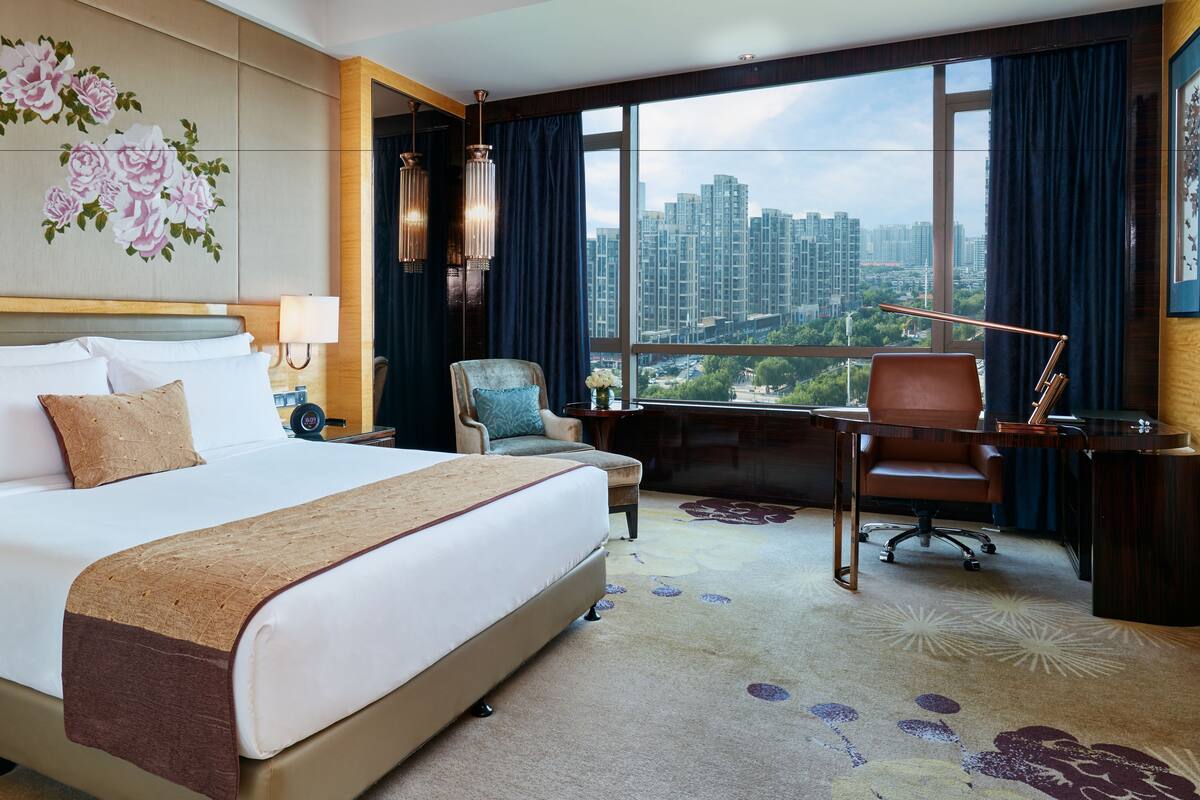 Een hotelkamer met een groot bed, een bureau, een stoel en uitzicht op een stadsgezicht.