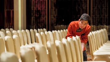 A person seated in a row of chairs in a room with a patterned wall.