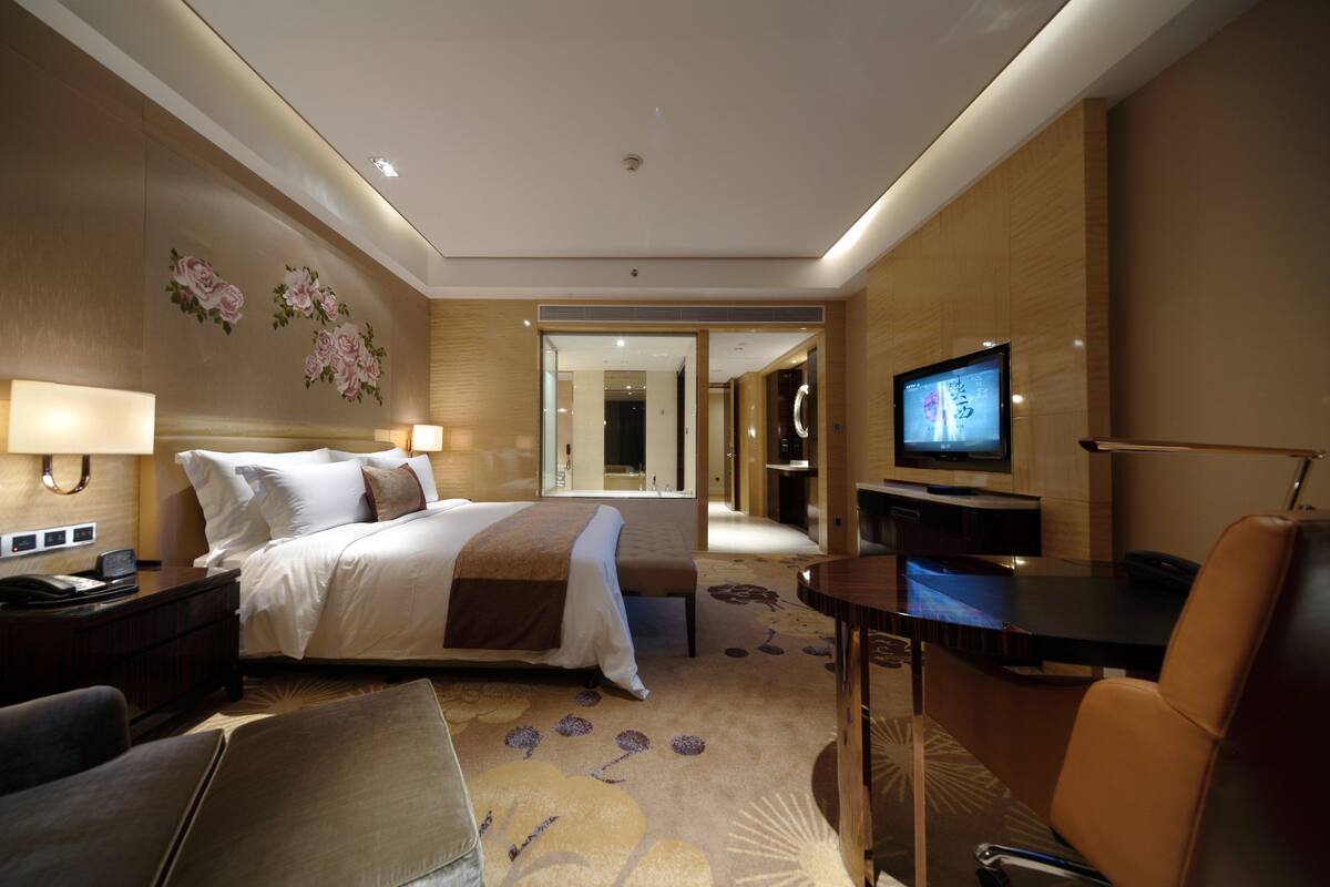 Een hotelkamer met een bed, nachtkastjes, een bureau, een stoel, een televisie en een badkamer zichtbaar door een geopende deur.