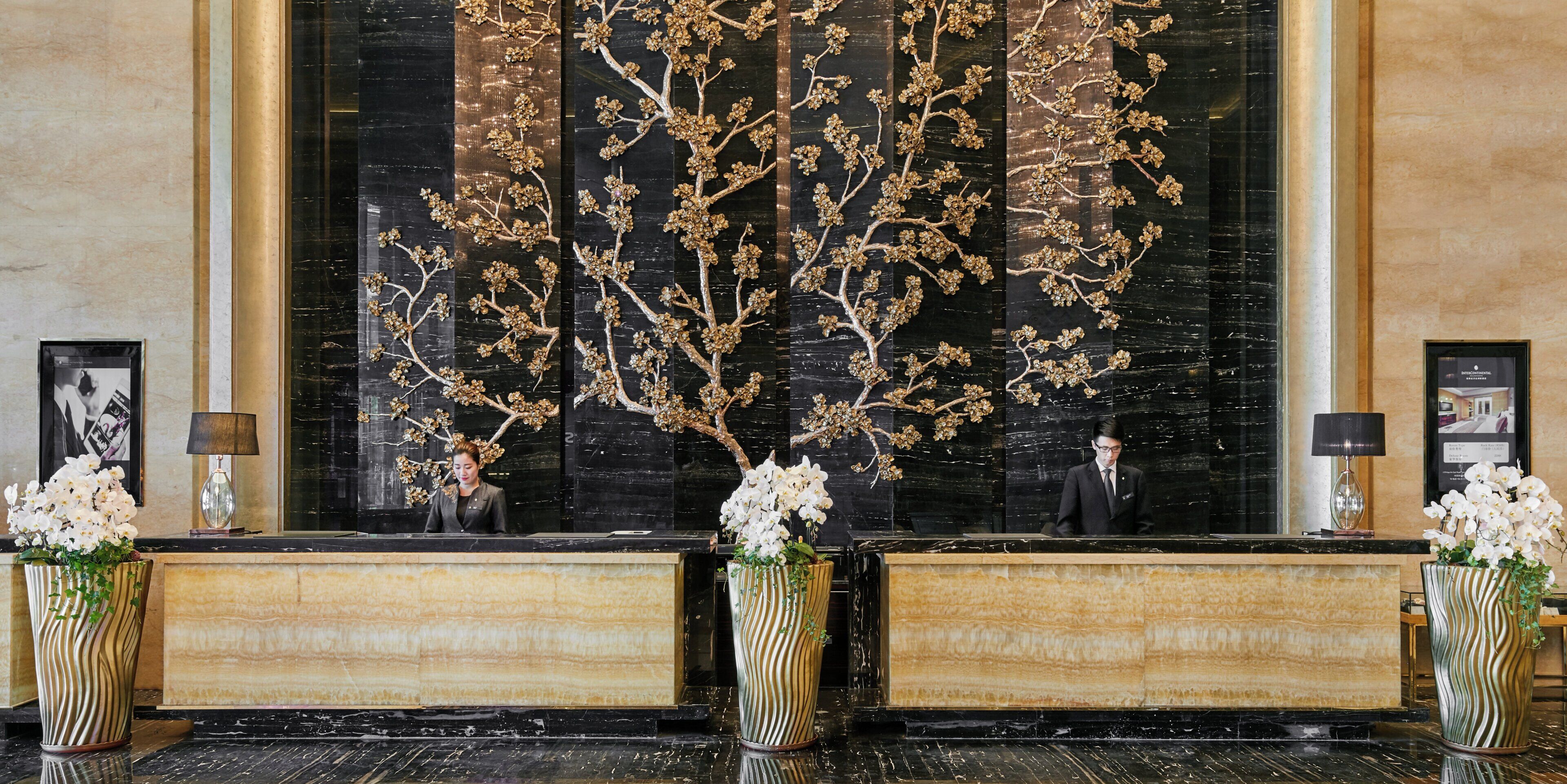 A reception desk with a large decorative tree mural, three vases with white flowers, and framed pictures on the wall.