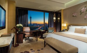 Une chambre d’hôtel avec un grand lit, un bureau avec une chaise, une télévision et une vue sur le paysage urbain.