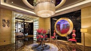 Un hall d'entrée luxueux, agrémenté d'un imposant lustre, d'un grand miroir rond et d'une enseigne traditionnelle indiquant la présence d'un restaurant chinois.