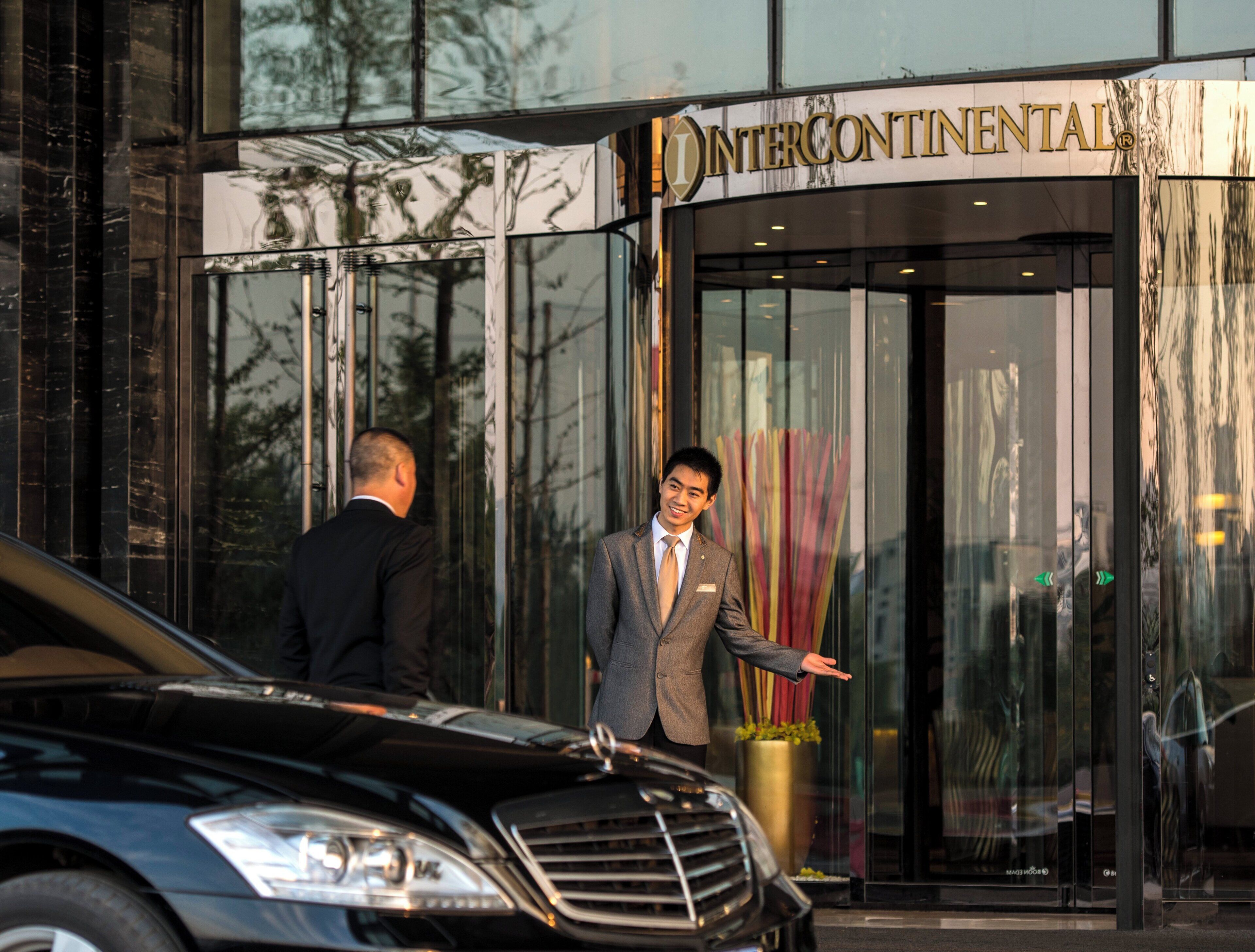 A man in a suit standing in front of a building with a glass entrance and a sign that reads 'INTERCONTINENTAL'.