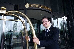 Een man in pak bij de ingang van een gebouw met een bord waarop ‘INTERCONTINENTAL’ staat.