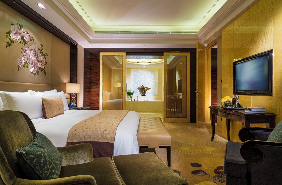 Quarto de hotel com uma cama grande, uma escrivaninha, televisão e banheiro visível por uma porta aberta.