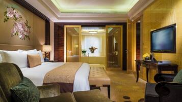 Quarto de hotel com uma cama grande, uma escrivaninha, televisão e banheiro visível por uma porta aberta.