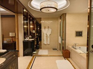 Een luxe badkamer met een grote spiegel, een kroonluchter, een badkuip en een badjas hangend aan de muur.