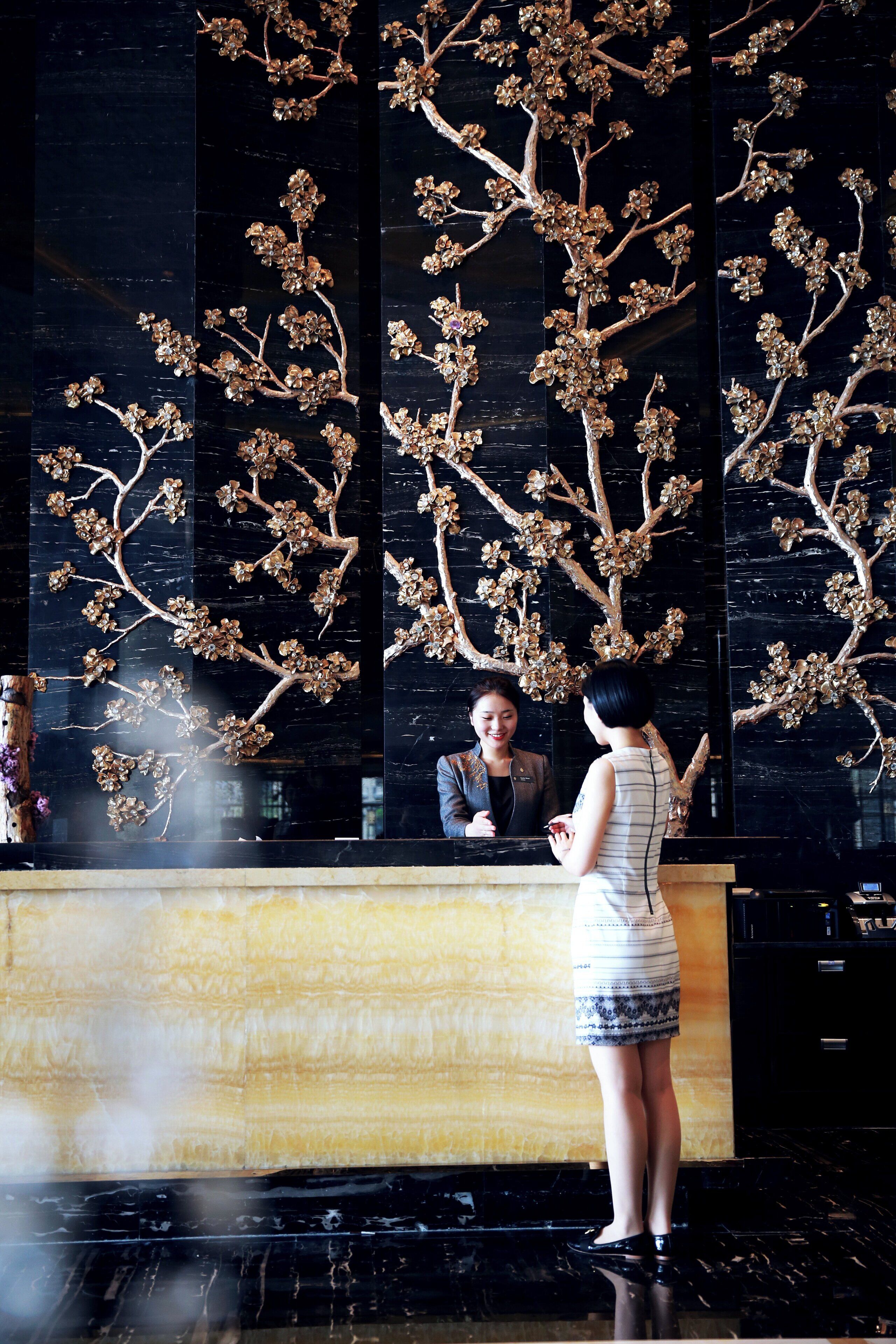 Un espace d’accueil avec un mur en marbre noir et une sculpture d’arbre décorative.