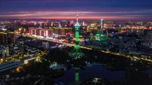 Un paisaje urbano nocturno con una torre destacada iluminada en verde, rodeada de edificios apretados y un río.