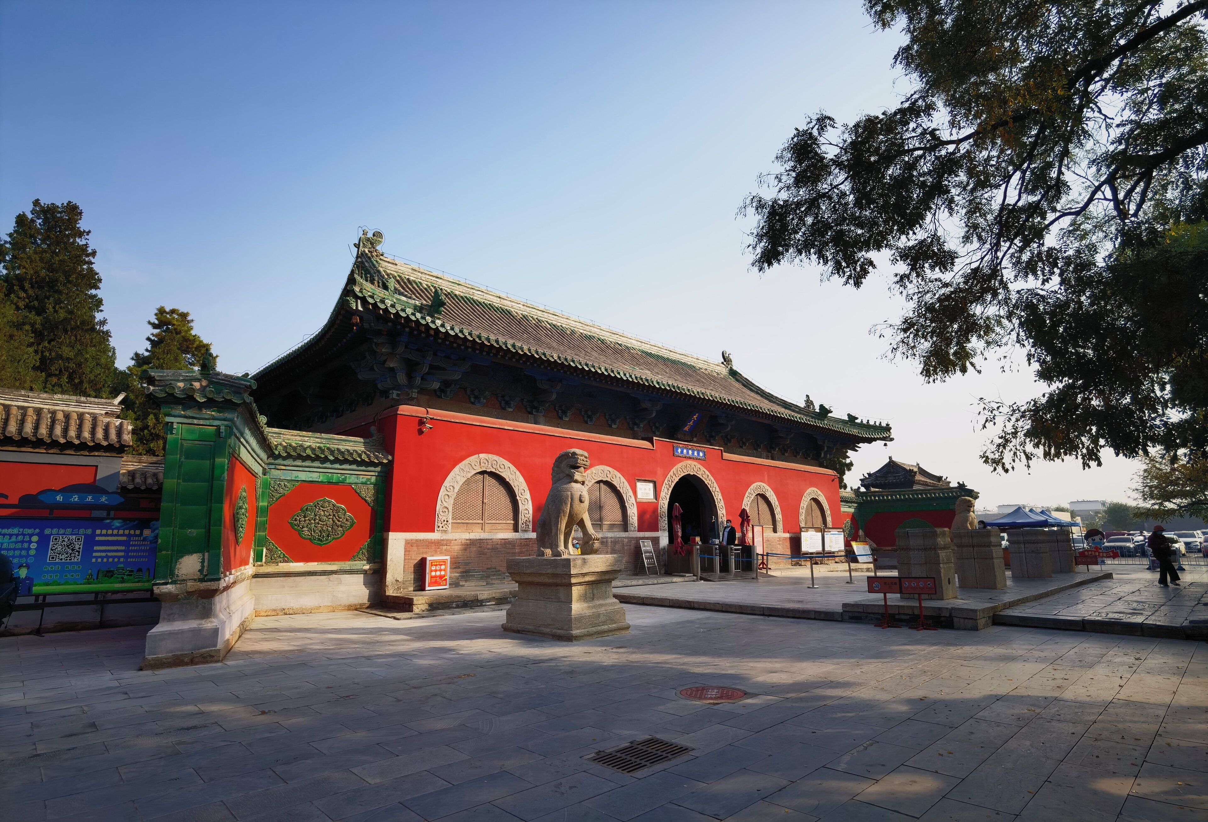 A traditional building with a tiled roof and arched doorways, surrounded by stone lion statues and a paved courtyard.