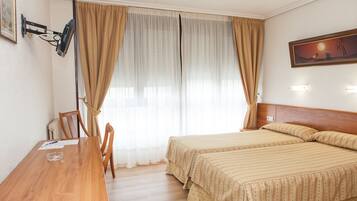 A hotel room with two beds, a wooden desk, and a chair.