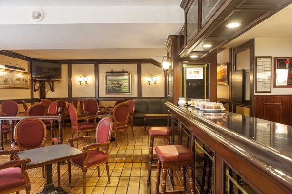 A restaurant with wooden tables and red chairs, a tiled floor, and wall-mounted light fixtures. - Hotel Las Anclas (El Astillero)