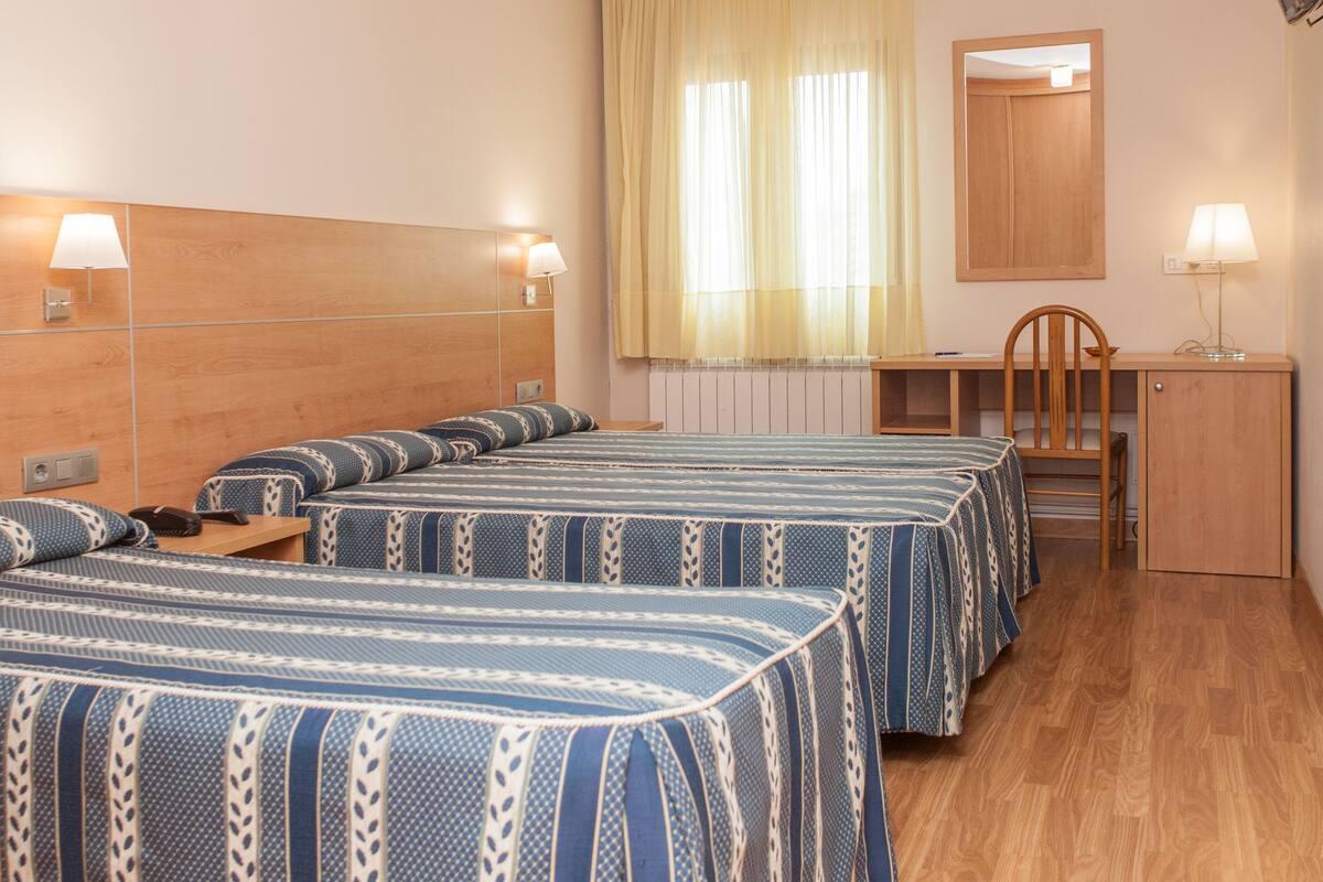 A hotel room with four beds, a wooden desk, a chair, a mirror, and two bedside lamps.