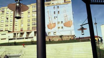 Un hotel con un mural de barcos en su fachada, una plaza de ladrillo rojo y un cielo azul despejado.