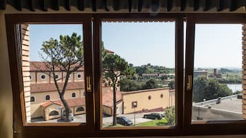 A window with a view of a building with a tiled roof and a tree in front.