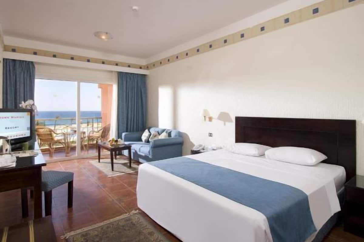 Una habitación de hotel con una cama, un escritorio, una silla, un televisor y vista al océano.