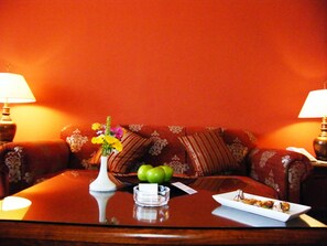 A room with a wooden coffee table, a vase with flowers, a plate with food, and a couch with patterned cushions.