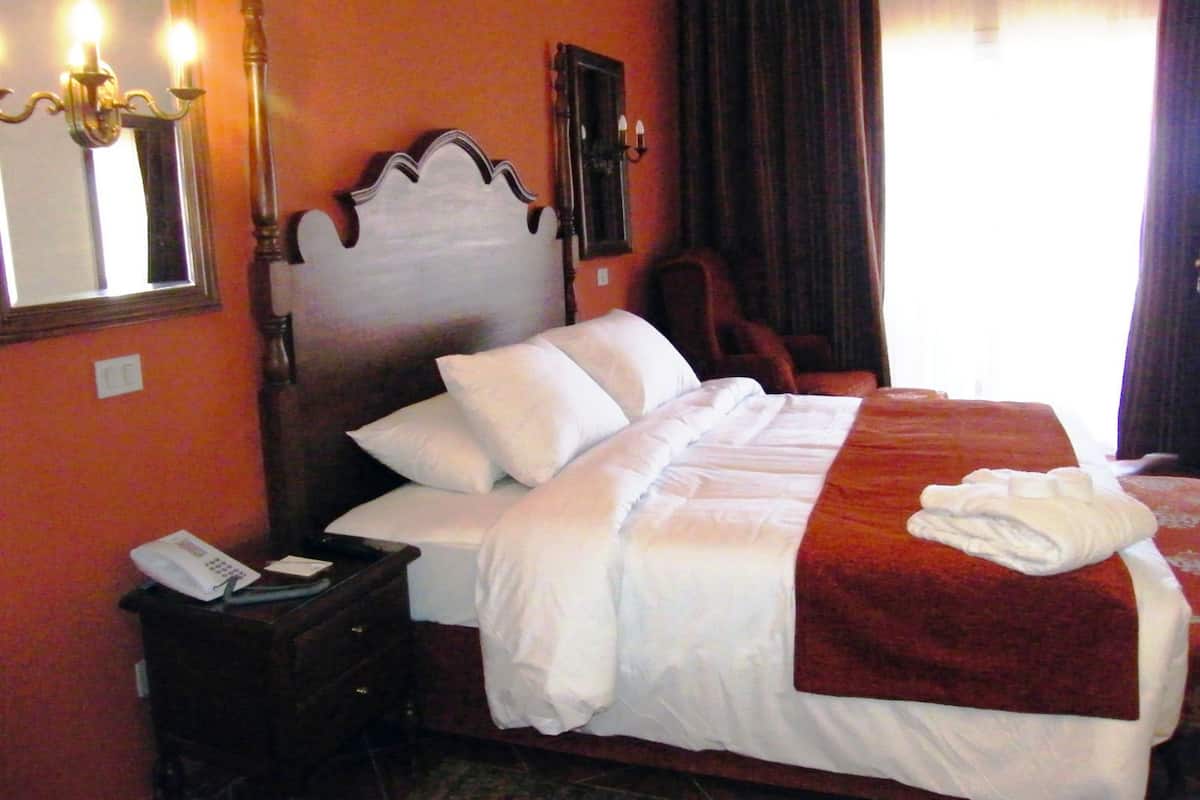 Habitación de hotel con una cama grande, una mesita de noche con teléfono, una silla y un espejo en la pared.