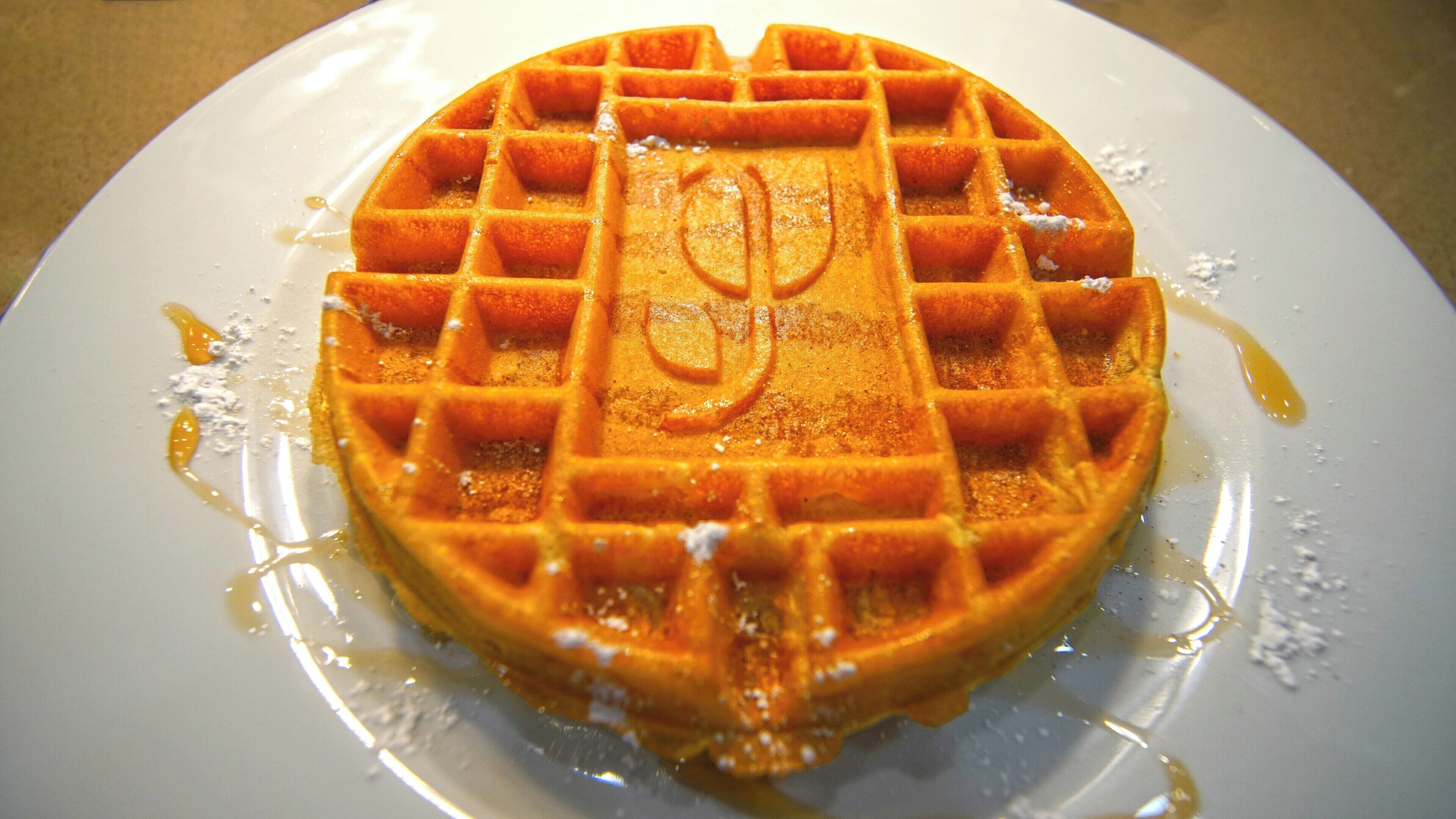 A waffle with syrup on a white plate.