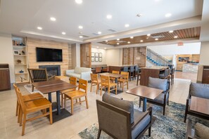 A hotel lobby with a fireplace, multiple seating areas, a staircase, and a television.