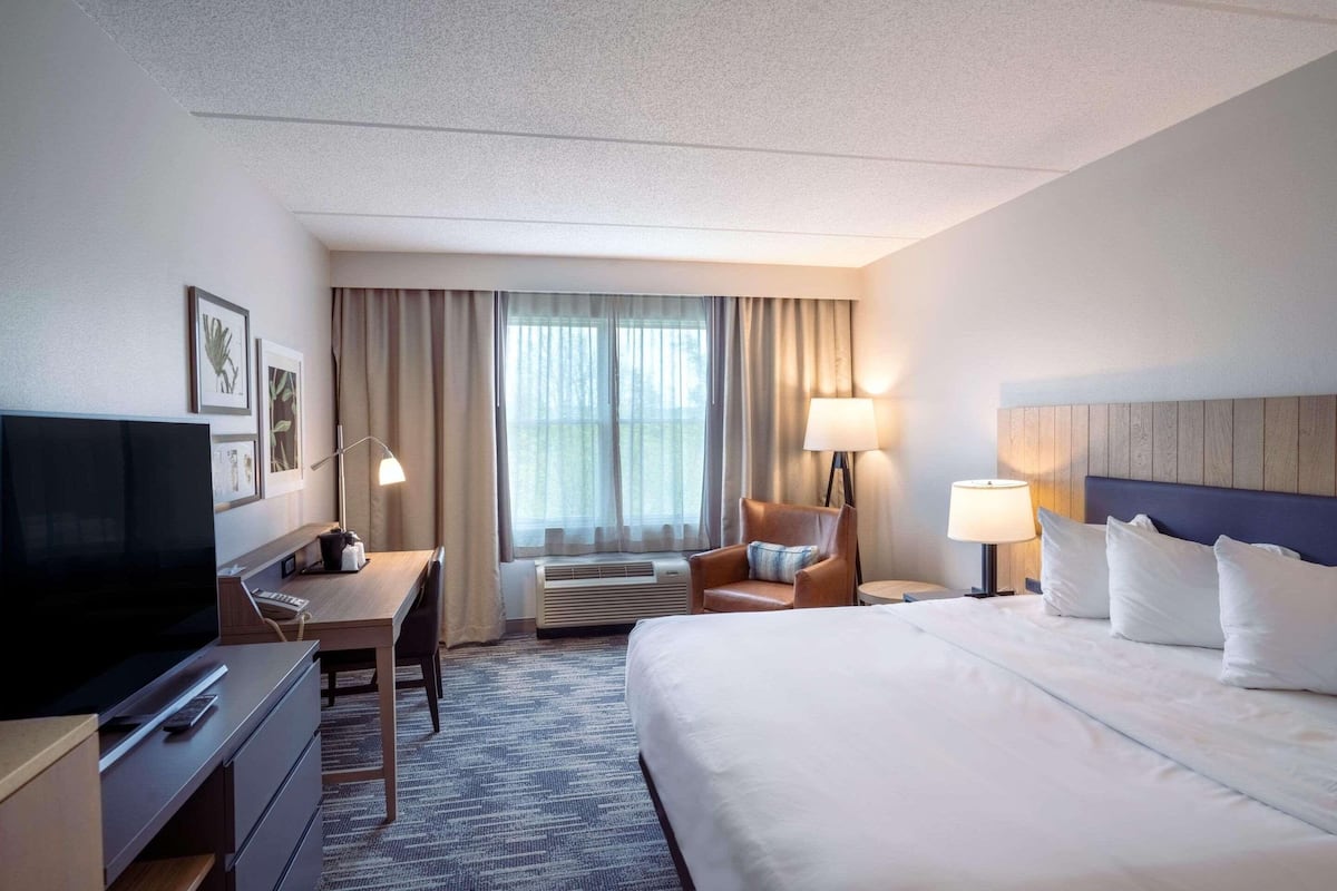 A hotel room with a large bed, a desk with a TV, a chair, and a window with curtains.