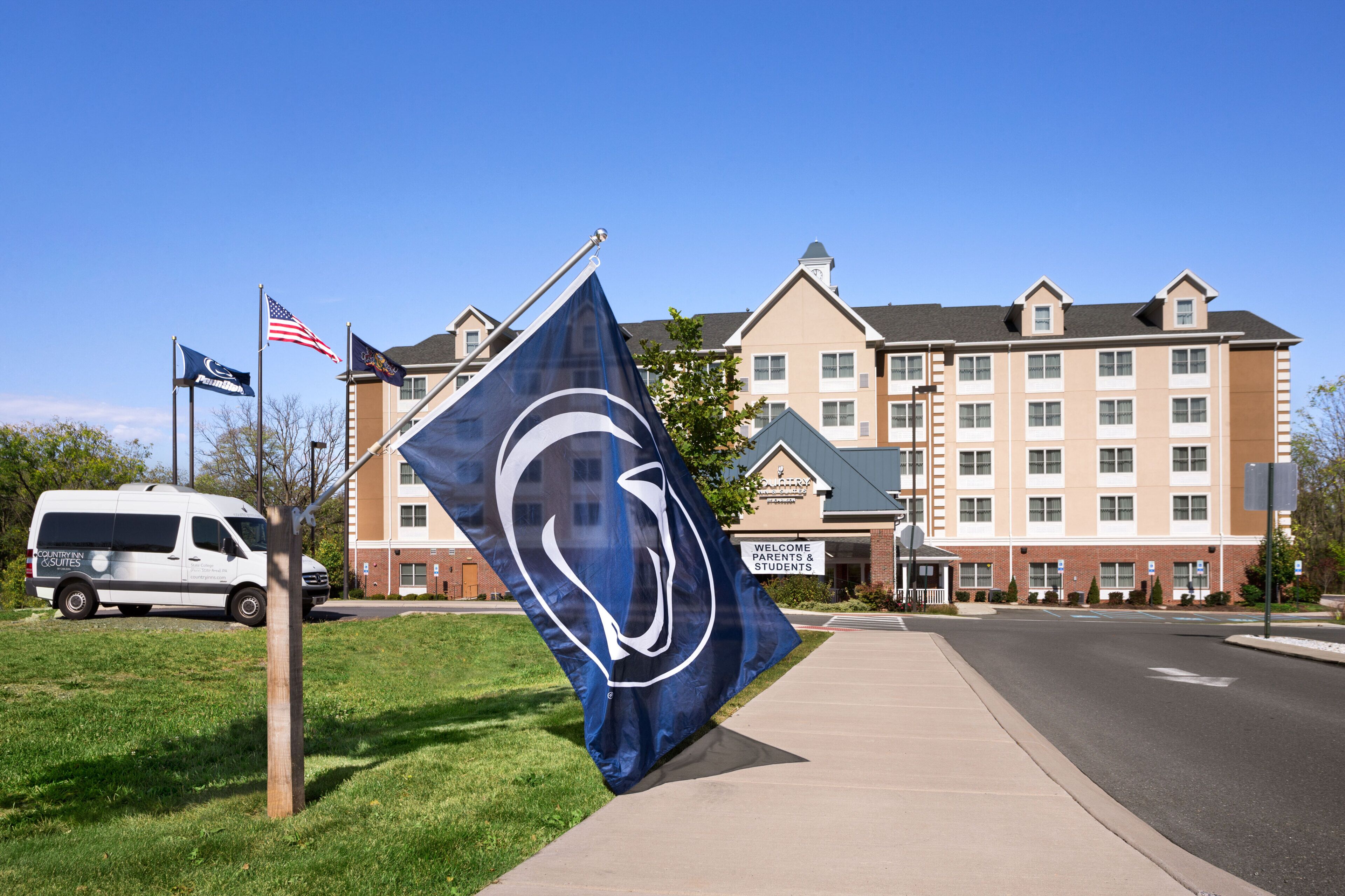 A hotel with a large flag, a van, and a sign welcoming parents and students.