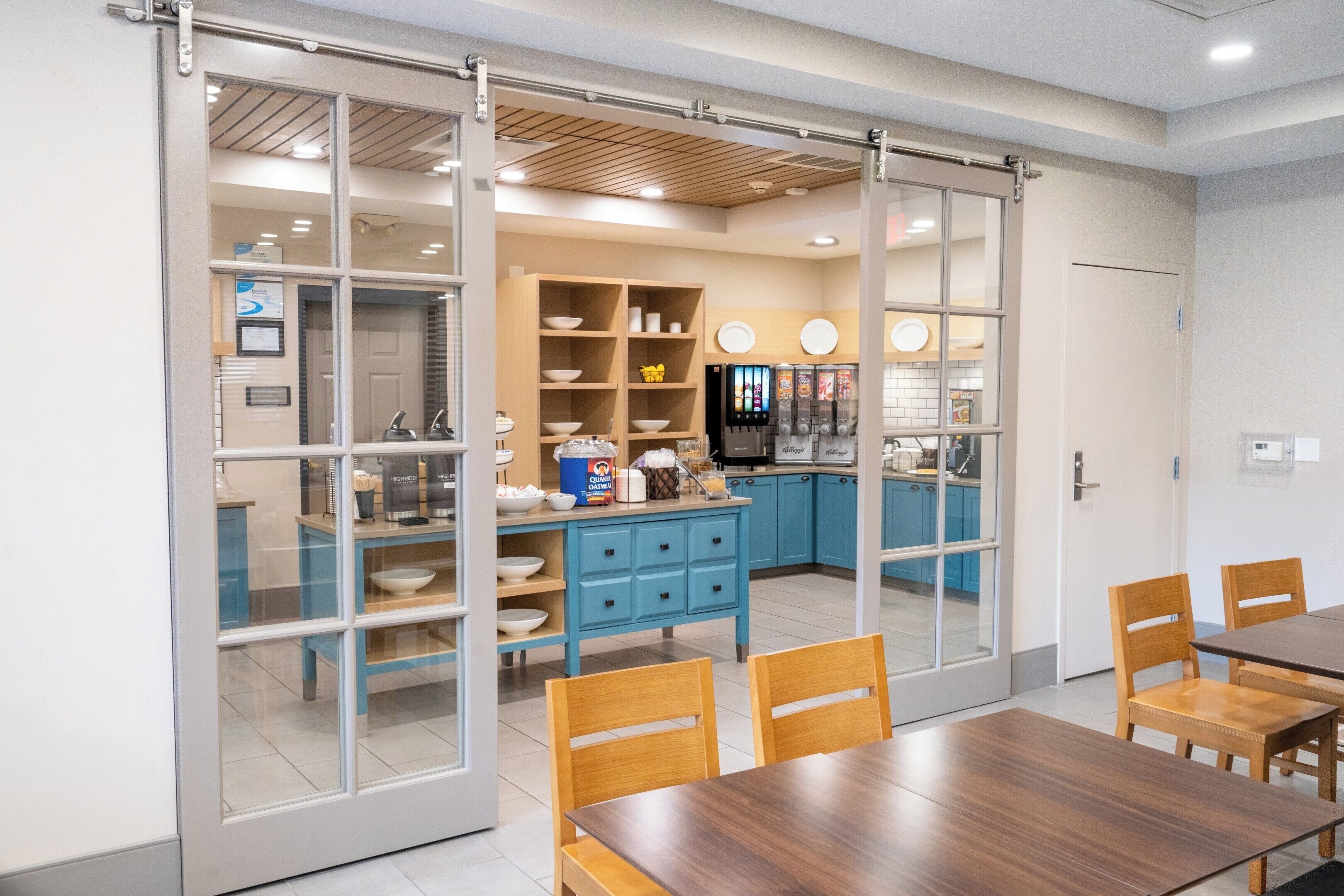 Una cocina moderna con armarios azules, una mesa de comedor de madera y un ventanal corredero que da a una zona de comedor.