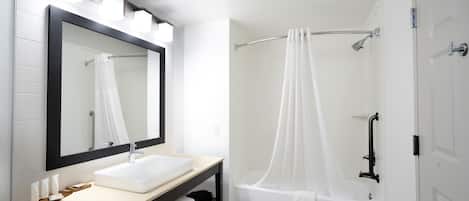 A bathroom with a white sink, a large mirror, a shower with a curtain, and a bathtub.