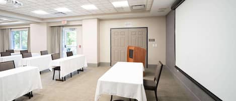 A conference room with tables, chairs, a projector, and a screen.