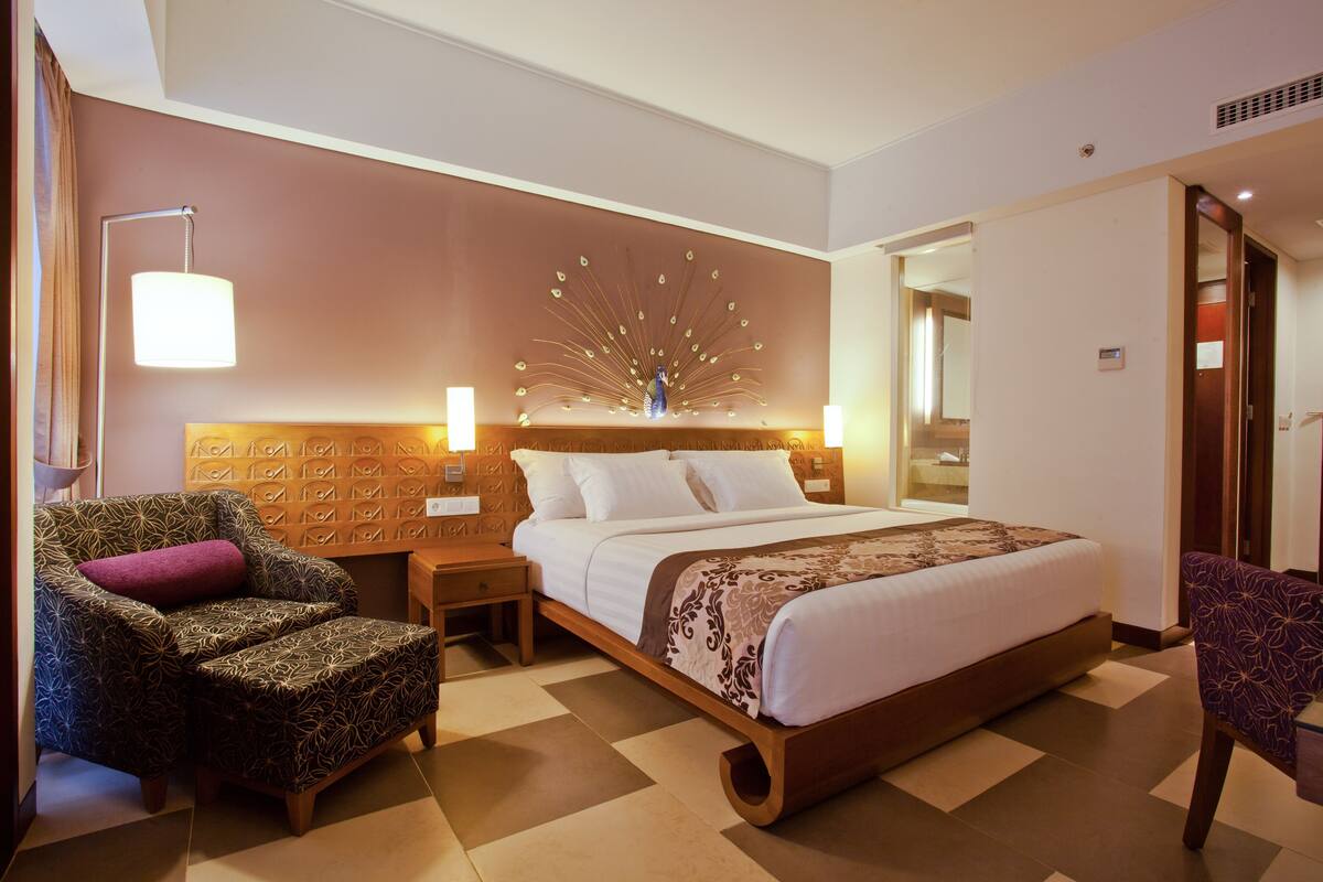 A hotel room with a large bed, two nightstands, a chair, and a decorative wall piece.