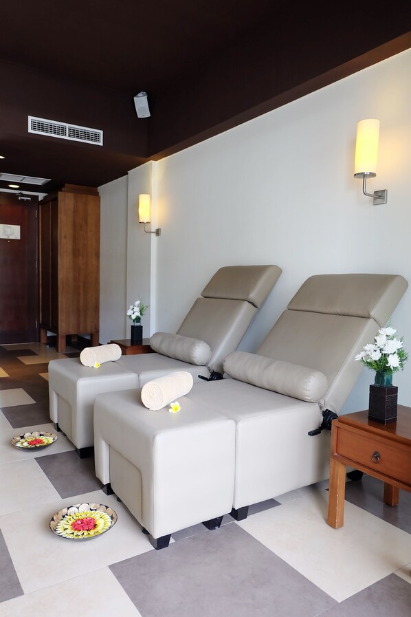 Un cuarto de spa con dos sillas de masaje, una mesita con un jarrón de flores y un plato decorativo en el suelo.