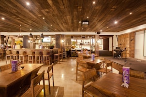 A restaurant with wooden tables and chairs, a bar area, and a stage with musical instruments.