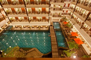 A multi-level hotel with a central swimming pool, balconies with plants, and outdoor seating areas.