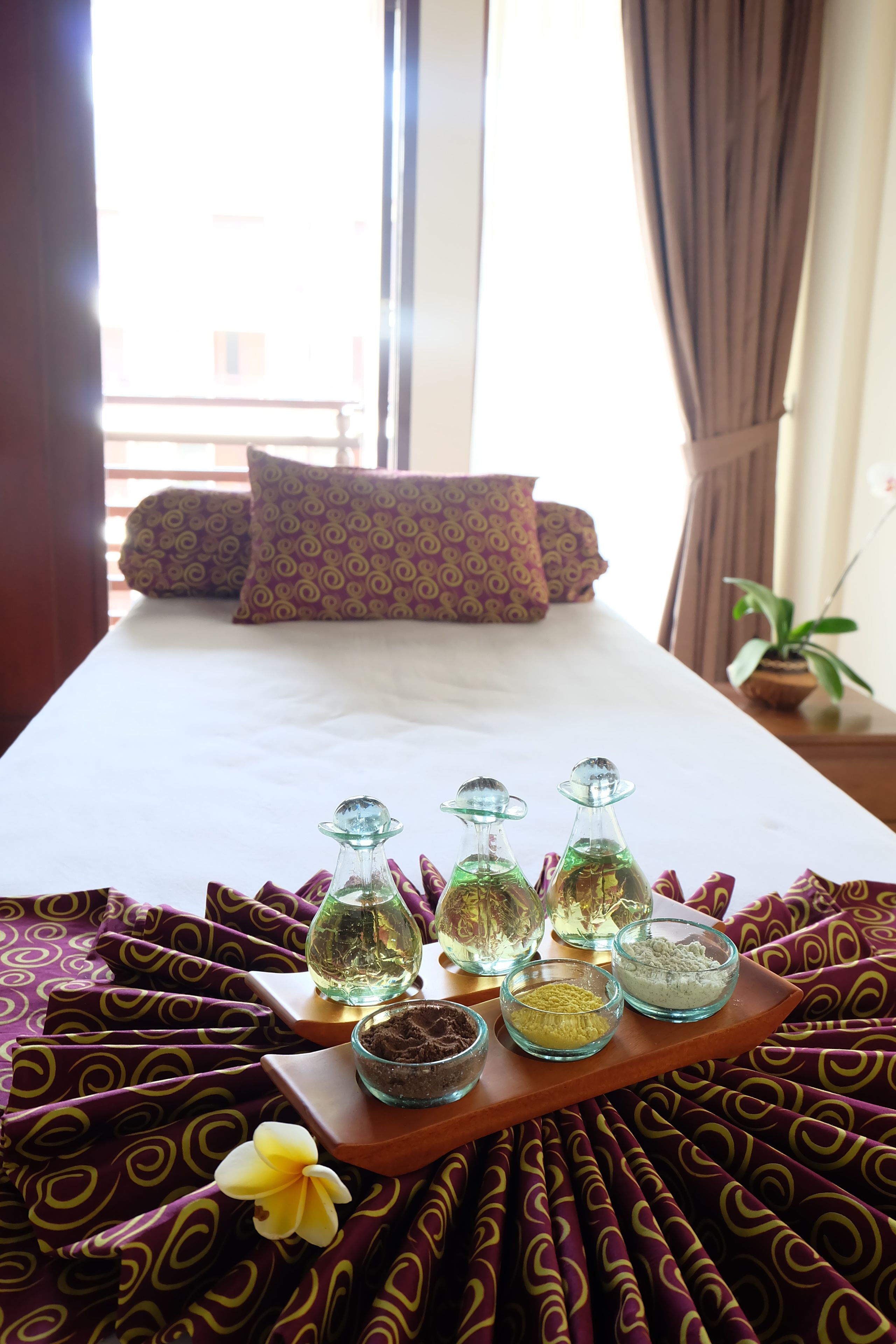 A neatly made bed with patterned pillows, a tray of toiletries, and a potted plant.