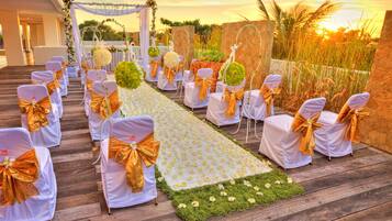 A wedding aisle with white chairs and gold sashes, decorated with flowers and greenery.