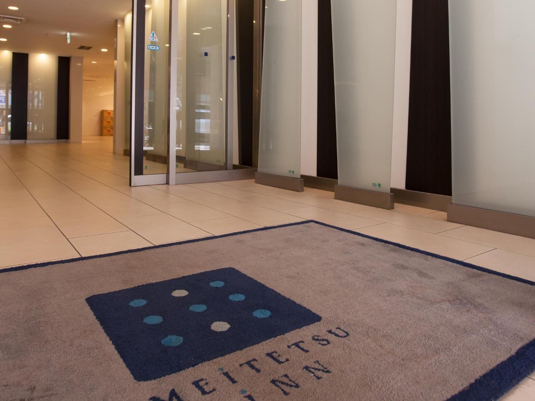 L’entrée d’un hôtel, avec un comptoir d’accueil, une porte vitrée et un tapis orné du nom de l’hôtel.