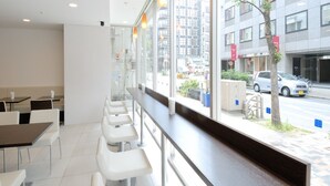 Un restaurant moderne avec un long comptoir et des chaises blanches, de grandes fenêtres offrant une vue sur la ville.