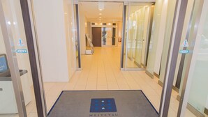 L’entrée d’un hôtel, avec un tapis bleu portant l’inscription « Meitetsu Inn » et une porte en verre.