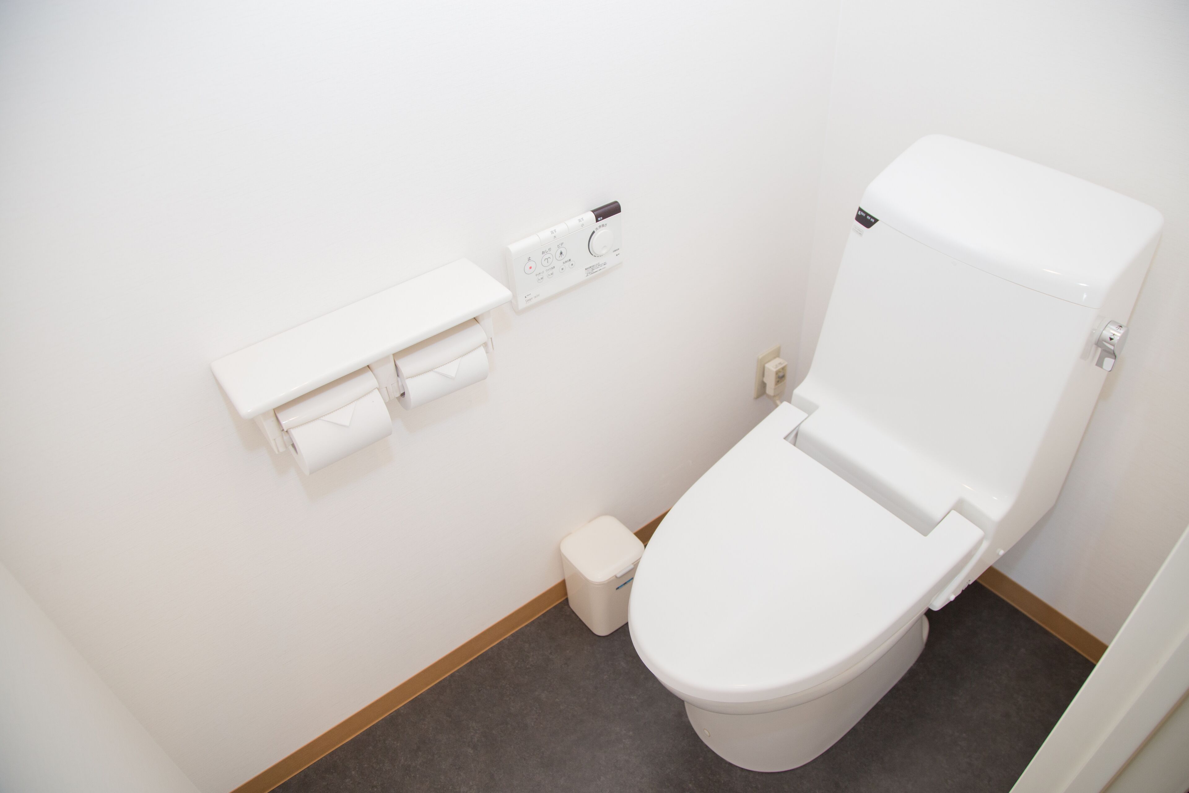 A white toilet with a flush handle, a toilet paper holder, and a small trash bin.