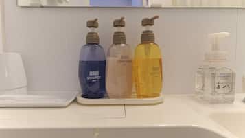 Un lavamanos de baño con tres botellas de champú y acondicionador, una botella de jabón corporal y un dispensador de desinfectante de manos.