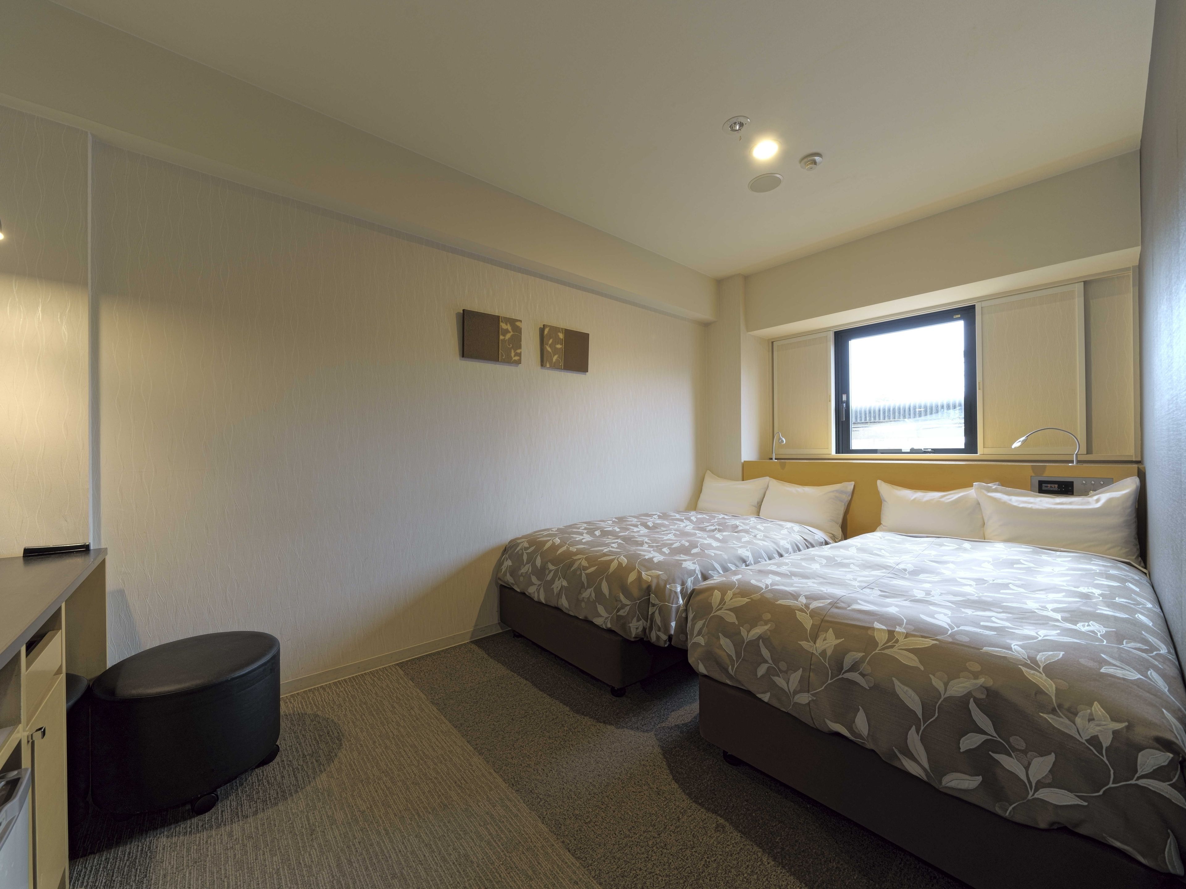 Habitación de hotel con dos camas, una mesita redonda pequeña, un aparador y una ventana con vistas.