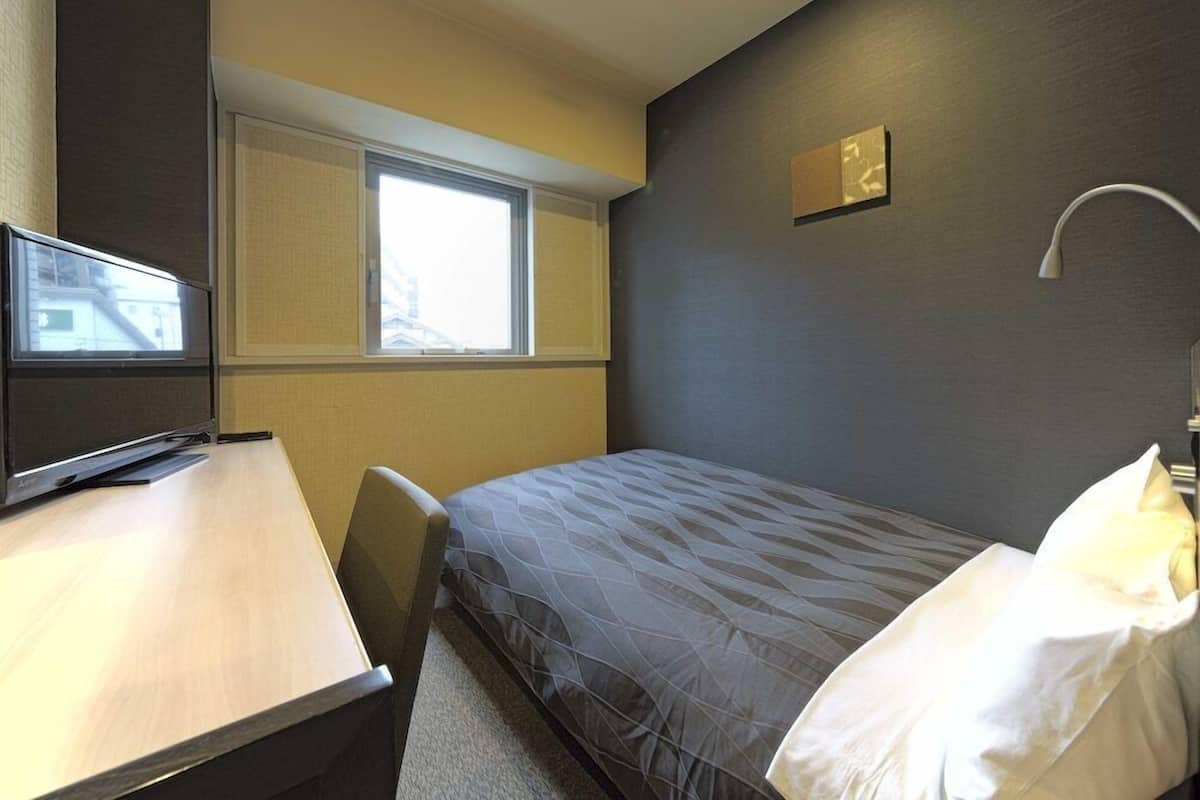 Quarto de hotel com cama, escrivaninha, cadeira, janela e luminária.