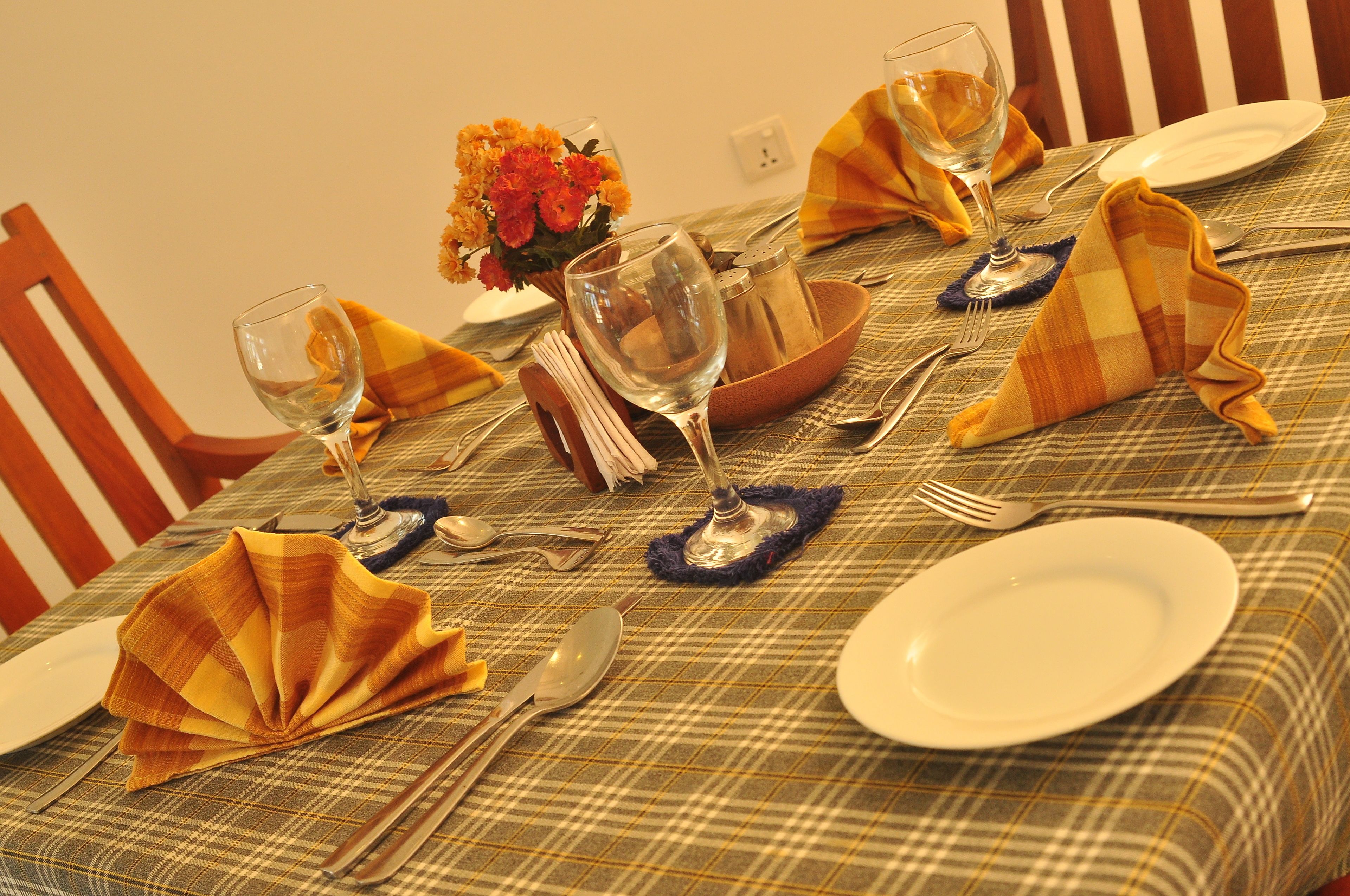 A dining table set with a plaid tablecloth, a vase of orange flowers, and neatly folded napkins.