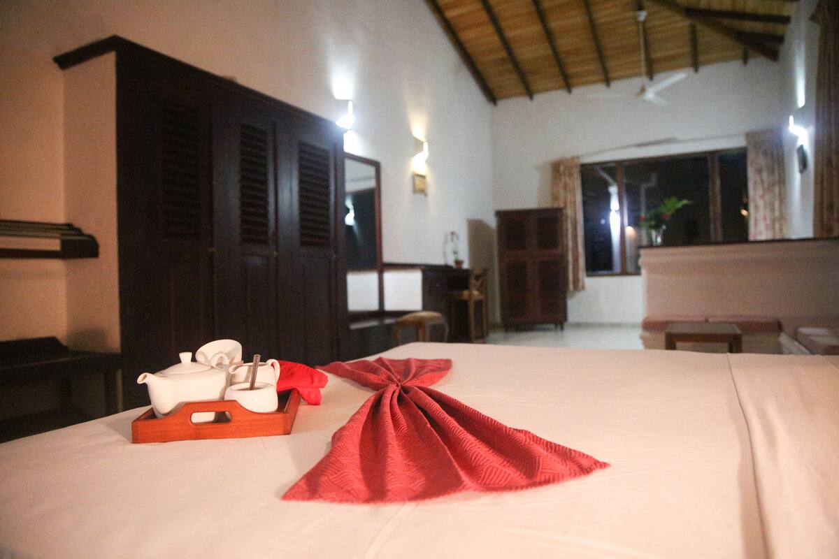 Habitación de hotel con cama, un armario de madera, una ventana con cortinas y una mesita con tetera y tazas.