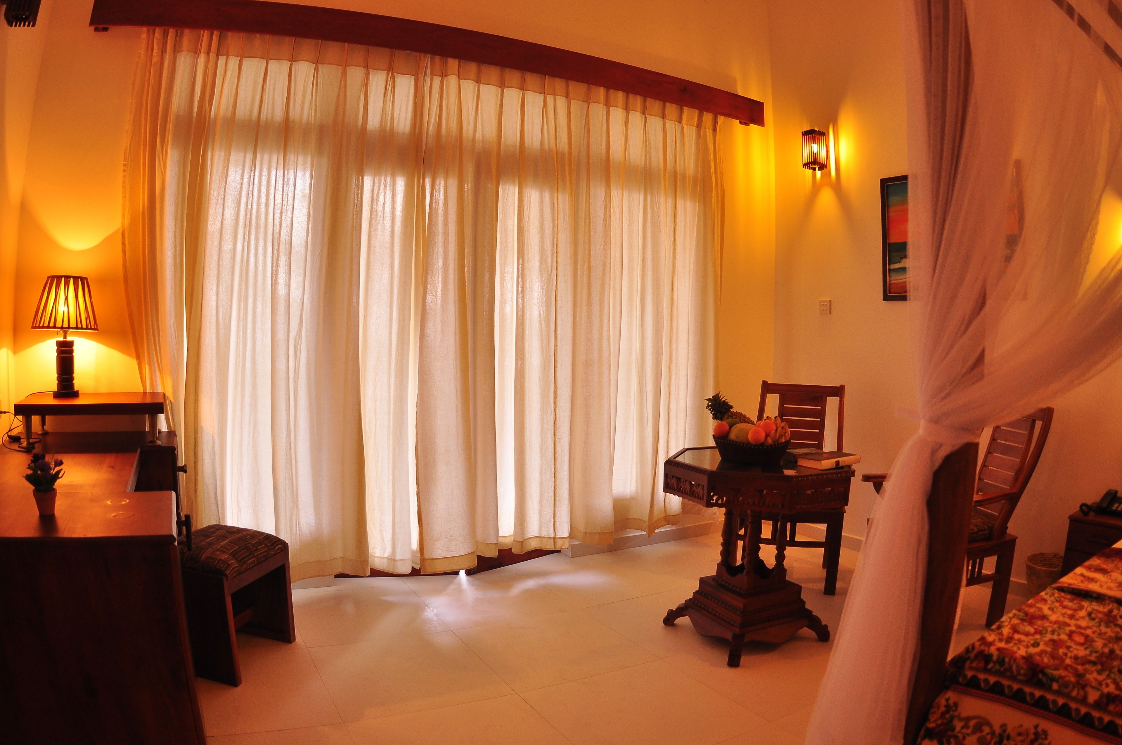 A room with a wooden desk, a chair, a small table with a pineapple, and a bed with a patterned bedspread.
