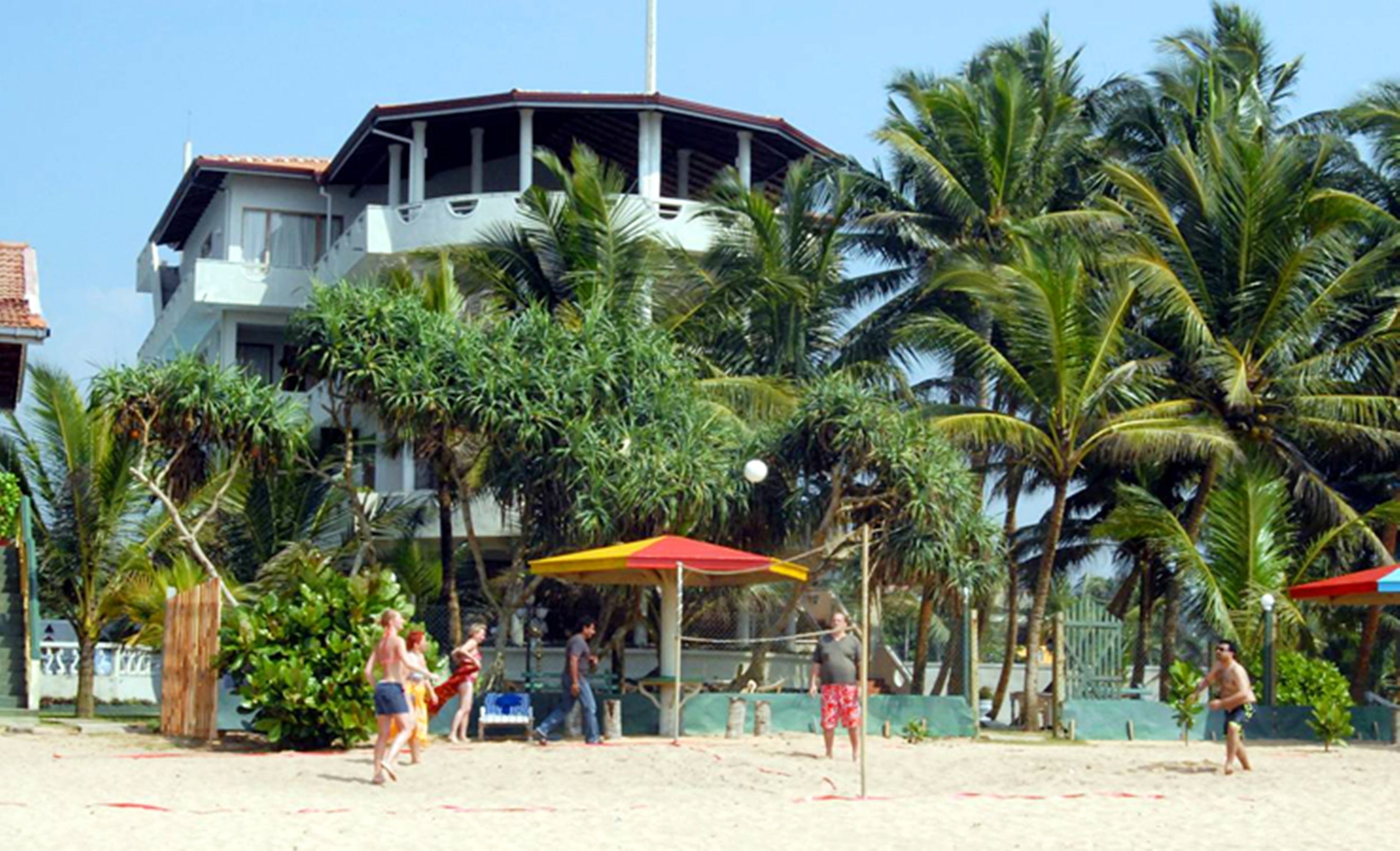 A beach volleyball court with palm trees and a large building in the background.