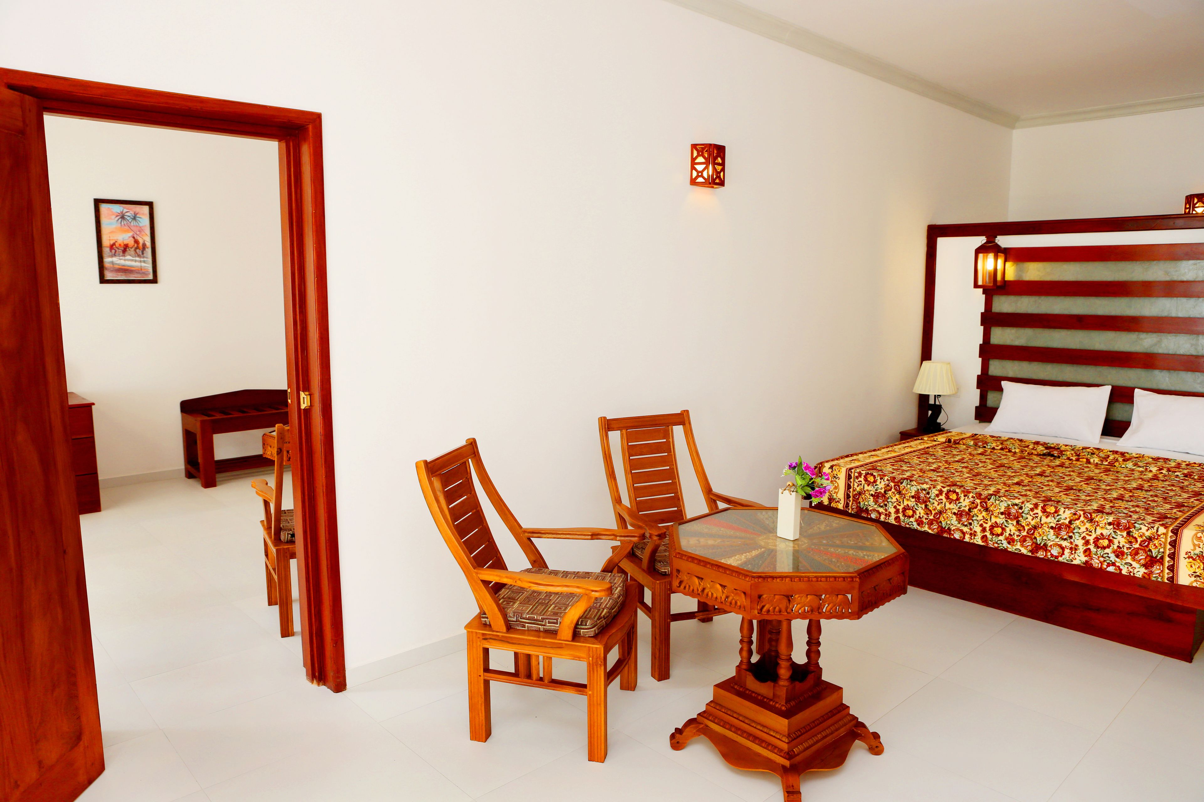 Une chambre d’hôtel avec un lit, une table à manger en bois avec des chaises, une petite table d’appoint et un tableau au mur.