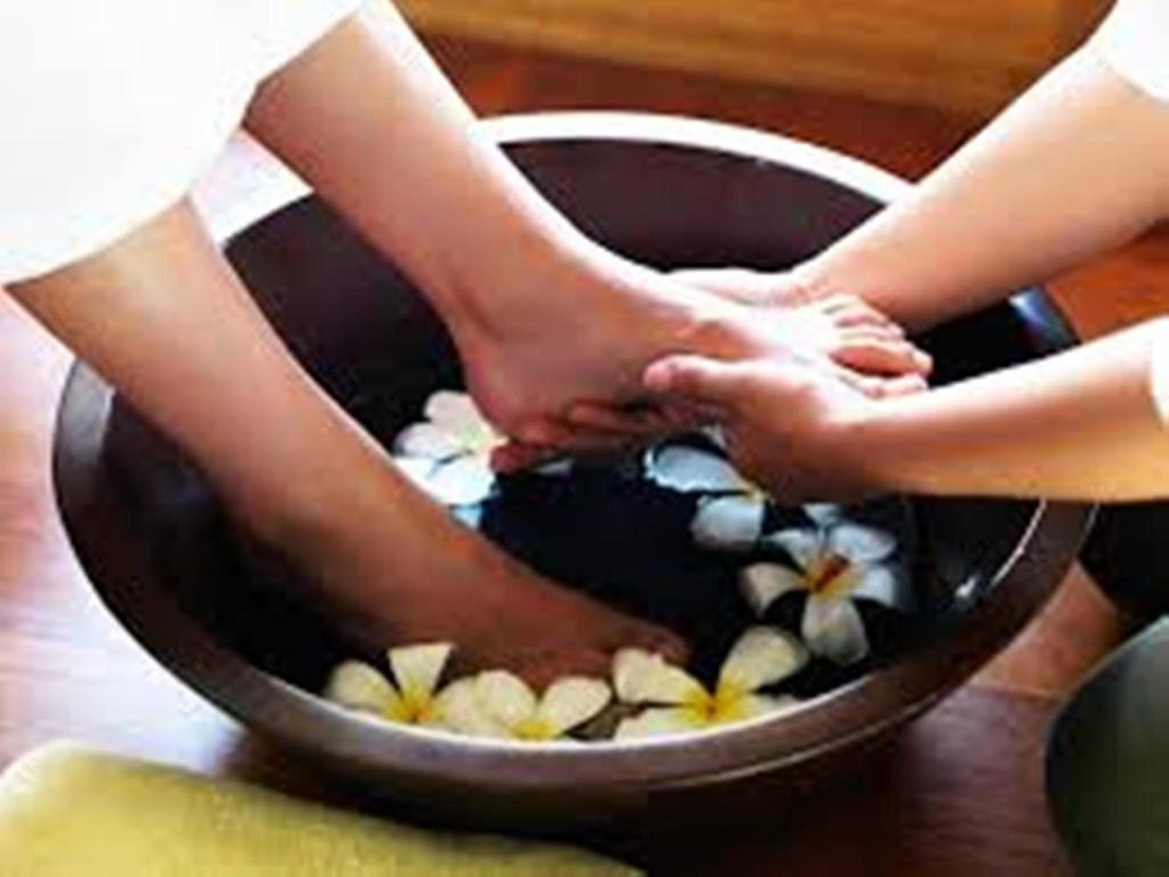 A wooden bowl filled with water and white flowers, likely used for a foot soak or spa treatment.