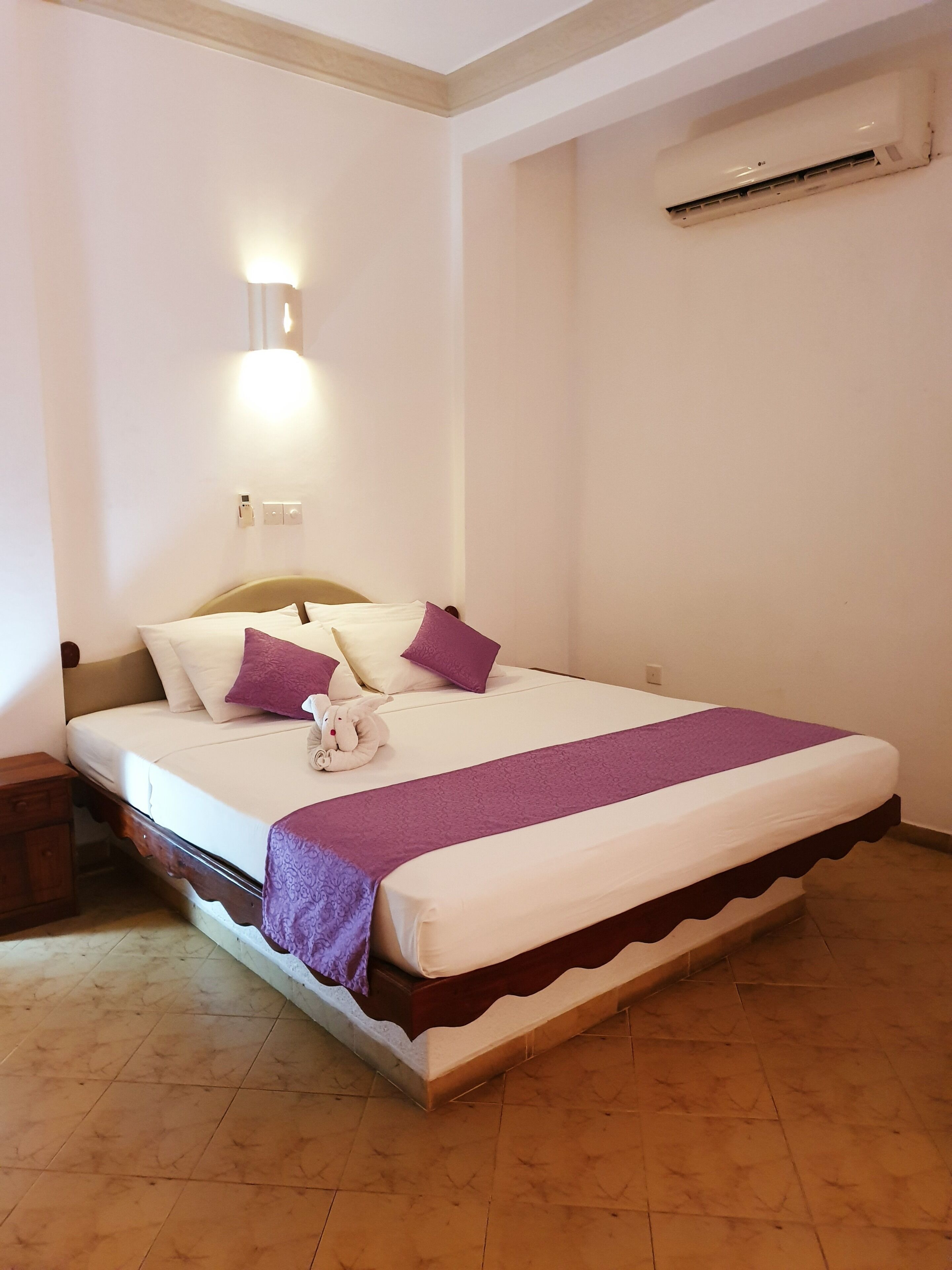 A neatly made bed with a headboard, a bedside table, and a wall-mounted air conditioner.